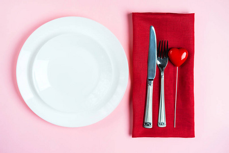 情人节的节日餐桌布置，粉红色的桌子背景上有叉子刀和心形图案。