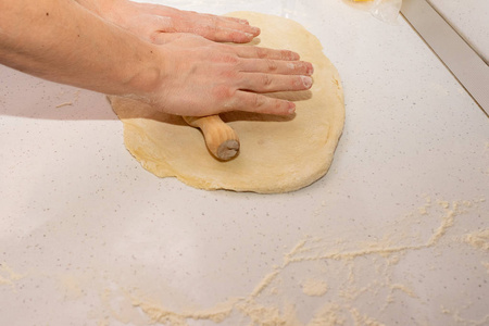 把面团擀开。面包师把面团放在厨房里撒了面粉的木桌子上