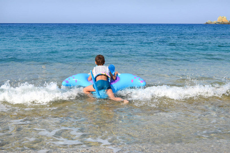 男孩穿着救生衣正在海里游泳，靠在蓝色的空气床垫上，使水飞溅，倒影