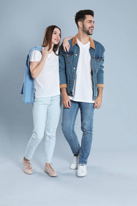 一对年轻夫妇穿着灰色背景的时髦牛仔裤