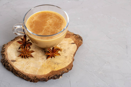 在一个木制托盘上的灰色背景下，用玻璃杯盛着茴香肉桂和生姜的玛萨拉茶