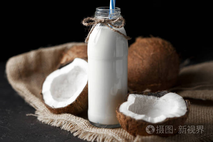 黑暗背景下的瓶装鲜椰奶黑桌子上的椰子奶昔