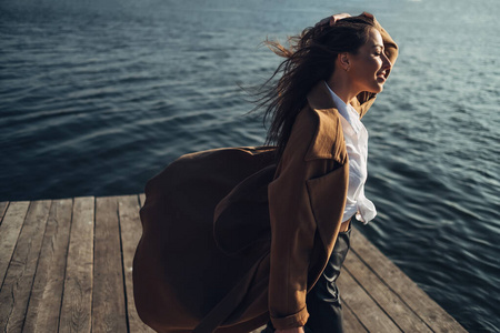 美丽的年轻时髦女孩穿着外套走在春天的海滩日落