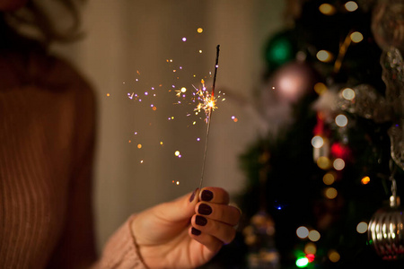 在黑暗的节日房间里，漂亮女人的手上闪耀着闪亮的火花。圣诞快乐，新年快乐。