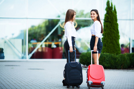 两个女孩一起拎着旅行箱在机场旅行。