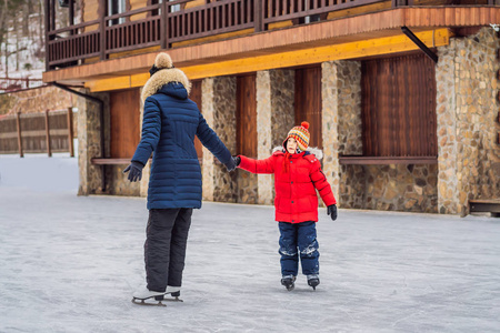 年轻的母亲在室外溜冰场教她的小儿子滑冰。一家人在户外溜冰场过冬