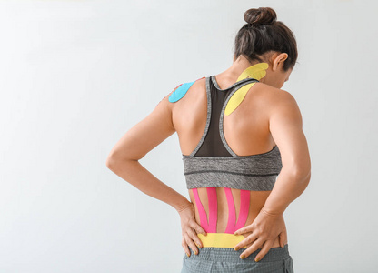 运动型女性，背部贴着理疗胶带，背景为浅色