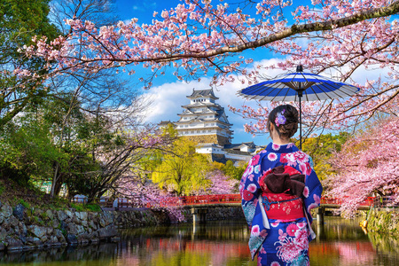 穿着日本传统和服的亚洲妇女看着樱花和城堡。