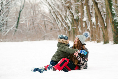 年轻的母子俩在冬季公园玩得很开心。一家人在户外玩雪。圣诞假期快乐。