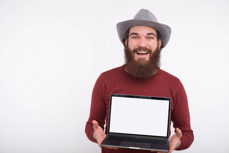 照片中，一位快乐的年轻胡须男子在笔记本电脑上显示空白屏幕，供复制空间使用