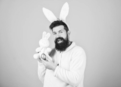 复活节兔子。穿着兔子套装的男人在玩玩具。有趣的兔子人耳朵柔软。复活节活动概念。还是孩子气。庆祝复活节。一个留着胡子的时髦小兔，长