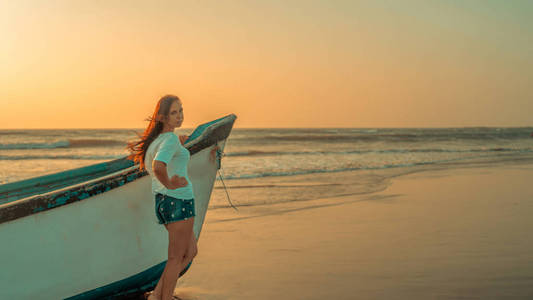 日落时，一个女人站在海边的船旁。d侧视图