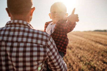 在阳光明媚的夕阳下，快乐的爸爸和他的小儿子在城外的田野里享受夏日的周末