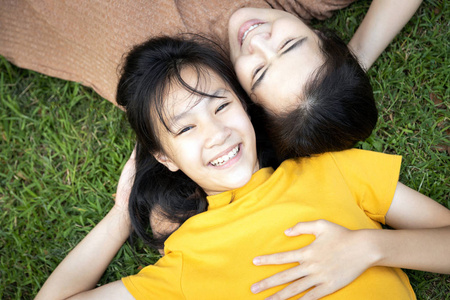 快乐的家庭，亚洲母亲和十几岁的女儿一起躺在绿色自然公园的草地上放松，亚洲女孩带着微笑，在假期里看着相机，保留着故事和记忆