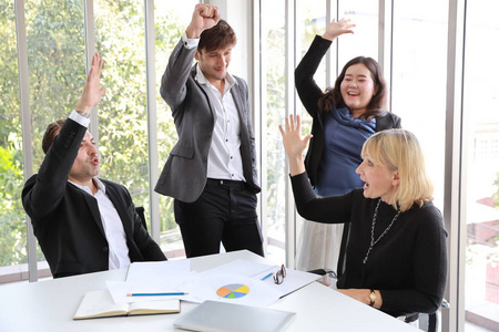 多民族商人在会议上展示成功的商业利润图，然后举手示意他们的工作就是成功，在会议室里笑脸盈盈