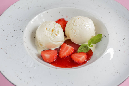 香草草莓冰淇淋与草莓和水果糖浆在一个白色盘子浅粉色背景。俯视图。