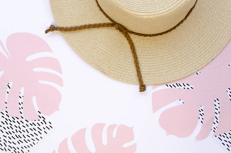 女性餐桌夏季概念。柳条帽和纸制怪物白色背景上的棕榈叶。粉红色柔和色调，俯视图