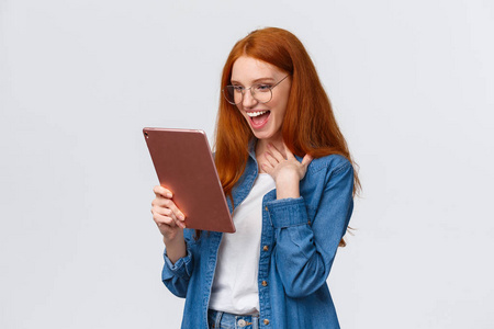 兴奋开心惊喜开朗的红发女朋友用小玩意发短信，拿着数码平板电脑，摸着胸脯欣喜若狂，笑出了响亮的设备屏幕