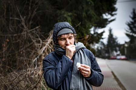 多云寒冷的日子里，一个生病咳嗽的男人走在街上。流感季节。感染。