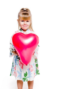 身穿印花连衣裙的小女孩手持白色背景上的红色心形气球