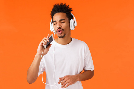 应用技术和智能手机概念。无忧无虑快乐的非洲裔美国男性玩卡拉OK游戏，应用，唱歌成移动麦克风，戴耳机，听音乐