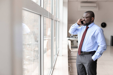 一位英俊的非裔美国商人在办公室的窗口边用手机聊天