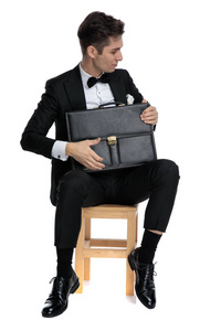 young elegant man in tuxedo holding suitcase 