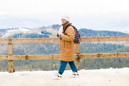 快乐的旅游老太太背着背包站在观景台上，看着美丽的山峦覆盖着积雪