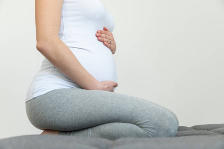 Young pregnant woman holds her belly sitting on a sofa  Gender 