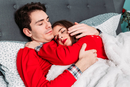 这对情侣穿着相配的红色睡衣躺在床上，拥抱着，看上去很幸福。