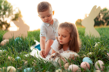 小男孩和女孩在玩兔子。快乐的小女孩抱着可爱的毛茸茸的小兔子。春天的照片与美丽的小女孩和男孩与他们的兔子