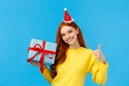 女孩可以很容易地包装你的礼物。喜怒无常的漂亮红发女店员帮顾客解决问题，伸出大拇指，做好或做好手势，微笑着拿着礼物盒