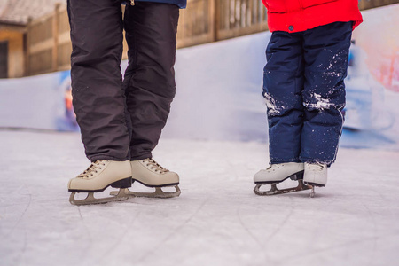 年轻的母亲在室外溜冰场教她的小儿子滑冰。一家人在户外溜冰场过冬