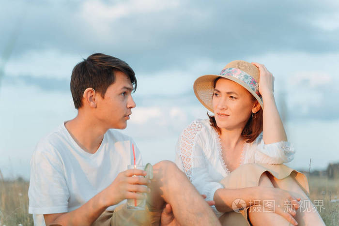 一个穿着白衬衫和帽子的漂亮女人和她的儿子坐在草地上聊天