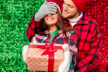 年轻人在彩色背景上用礼物遮住女友的眼睛