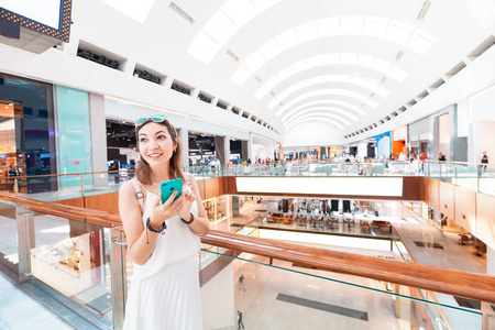 快乐的亚洲女孩在她的智能手机上收到一份带有折扣的营销时事通讯。在购物中心内部进行有利可图的现代购物