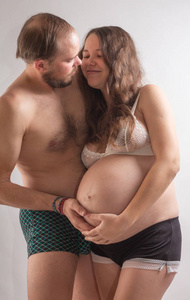 美丽的孕妇和她英俊的丈夫在床上一起亲吻。