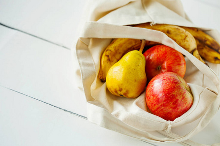 新鲜的有机水果用环保棉和织物包装，在白色木制餐桌上制作袋子