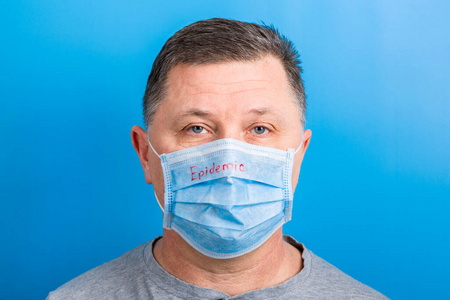 戴着医用面具的男人的肖像，蓝色背景上有流行语。冠状病毒概念。呼吸防护