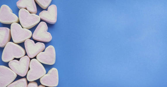 粉红色的心形棉花糖堆叠在时尚的蓝色背景上，带有复印空间。甜蜜的爱情糖果主题情人节概念。粉彩甜点作为背景或墙纸装饰