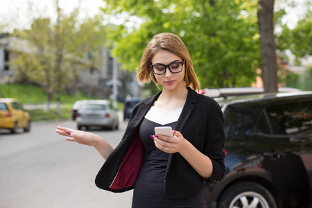 一个女人一边打电话一边发短信。半身女孩儿看着手机手机兴致勃勃地笑着站在户外城市背景下用手停车