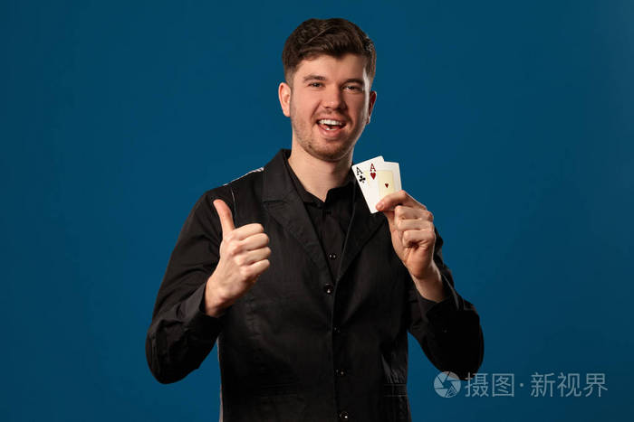 打扑克穿黑色背心和衬衫的人拿着两张扑克牌在蓝色工作室背景下摆姿势