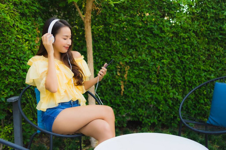 年轻的亚洲女人用智能手机和耳机给李