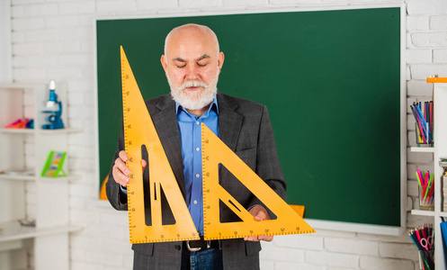 数学考试。黑板上的数学。高级男教师使用数学三角形工具。有胡子的老师在黑板前。回到学校。数学科学概念与学校课程项目