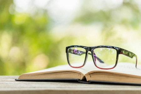 Book and eye glasses on wooden table with abstract green nature 