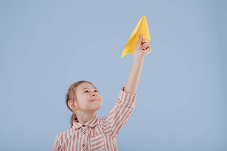 girl plays with yellow paper plane, looks at the camera, 