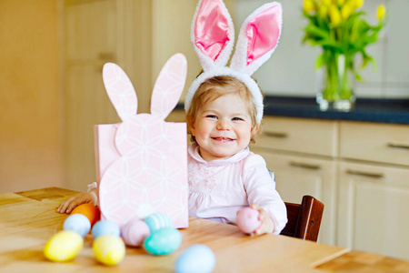 可爱的小女孩戴着复活节兔子耳朵玩彩色彩蛋。快乐宝宝打开礼物。穿着粉红色衣服的可爱的孩子在享受假期