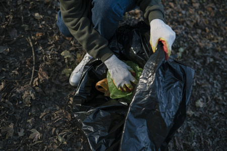 一个女人在落叶上收集垃圾，特写。生态系统污染，森林中的塑料垃圾