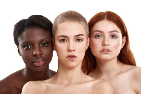 不同类型的皮肤。三个美丽的多元文化的年轻女子拥抱和看着相机，而站在工作室彼此靠近白色背景