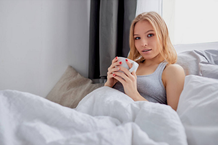 可爱的女人躺在床上喝一杯咖啡或茶